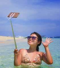 young beautiful and happy Asian Chinese woman having fun on sea water taking selfie picture with mobile phone camera on paradise beach