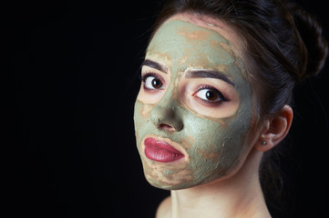 Closeup of young woman with cosmetic mask on the face on a dark background