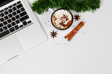 Flat lay home office desk workspace with laptop, a cup of hot chocolate topping with marshmallow and gift box on white background. Top view. Christmas background.