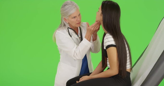 An older doctor gives a check-up to a young girl on green screen. On green screen to be keyed or composited. 