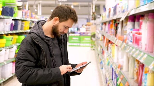 Young man chooses household chemicals in the supermarket. 