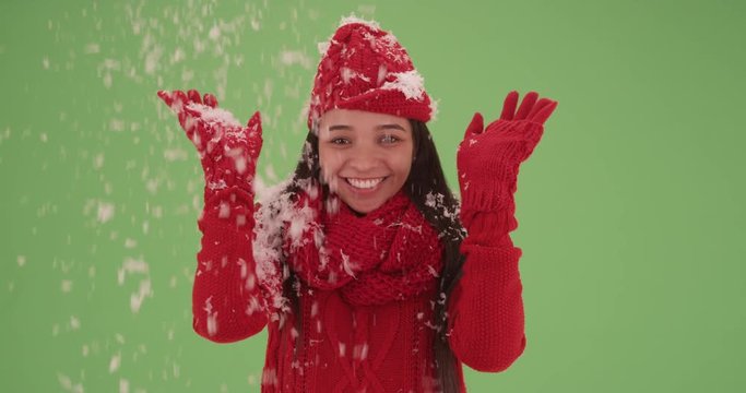 Happy smiling Hispanic girl in bright red winter clothes covered in snow on green screen. On green screen to be keyed or composited. 
