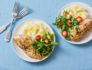 Baked chicken breast with mashed potatoes and arugula, celery, tomato salad on a blue background, top view