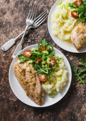 Mashed potatoes, baked garlic chicken breast and arugula, cherry tomatoes salad. Healthy food concept. Delicious lunch on wooden background, top view. Flat lay