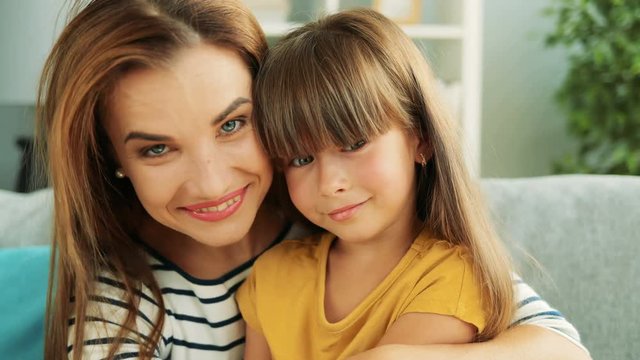Portrait of beautiful mother holding her cute little daughter on her knees and they smiling. At home. Close up. Indoor