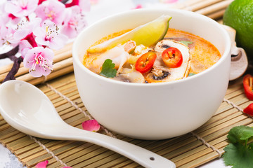 Traditional Tom Yum soup with blooming sakura branch on white stone table