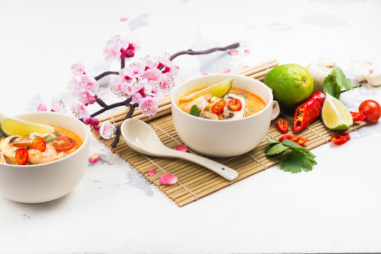 Traditional Tom Yum soup with blooming sakura branch on white stone table