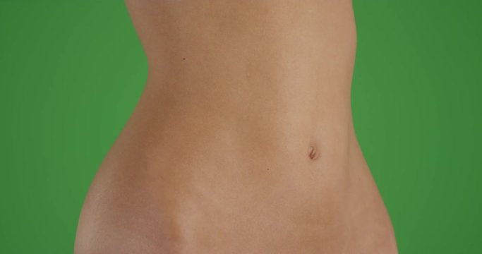 Midsection of a young millennial White girl on a greenscreen studio background. Stomach of attractive woman standing over Chroma key.