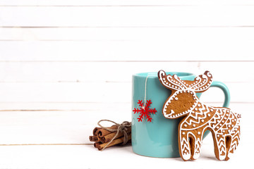 Mug of winter tea with gingerbread deer and cinnamon sticks on white wooden table. Copy space.
