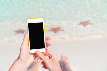 Closeup smartphone in female hands on the background of turquoise ocean at tropical beach