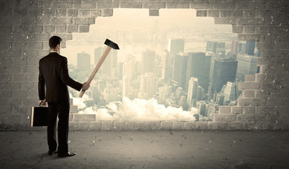 Business man hitting wall with hammer on city view