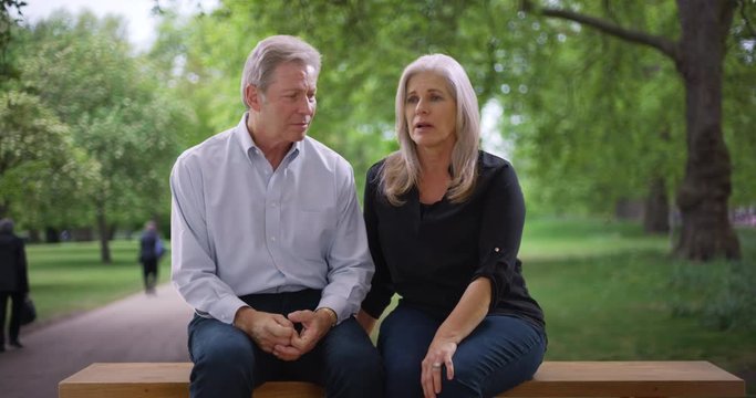 Old Caucasian Couple Sitting On Bench Have A Serious Talk In Public Park 