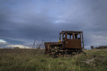 Fototapeta premium rusty and forgotten tractors stranded and left in the levels ruined by time. an old machine abandoned in the field of a dramatic blue sky background.