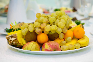 A dish assortment of fruit on a white tablecloth. Useful vitamin food. Vegetarian delicious meats. Festive meal for invited guests. 