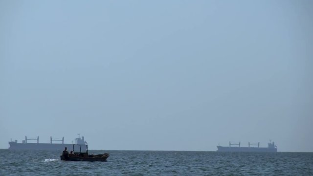 Boat and cargo ships. Fishing boat on the background of large ships.