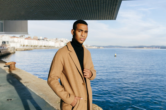 Black man in stylish coat at embankment