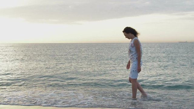 A happy woman walks in the sea at dawn.