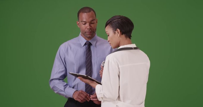 A black doctor advises an African American patient using her tablet on green screen. On green screen to be keyed or composited. 