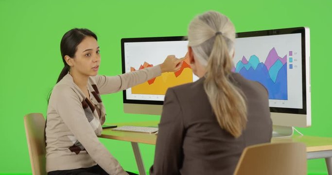 Two businesswomen discuss graphs on green screen. On green screen to be keyed or composited. 