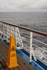 Obraz premium Safety warning marker on Teak lined Promenade Deck of modern cruise ship on a grey stormy day.