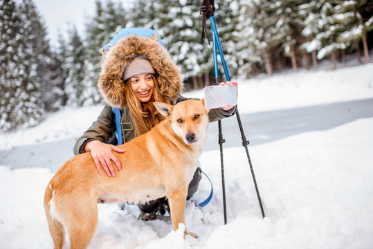 Woman having a break during the winter hiking making selfie with her dog at the snowy mountains near the lake and forest