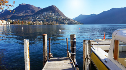 View of a pier on the lake on sunny day with mountains on the background, Lake Lugano, Italy