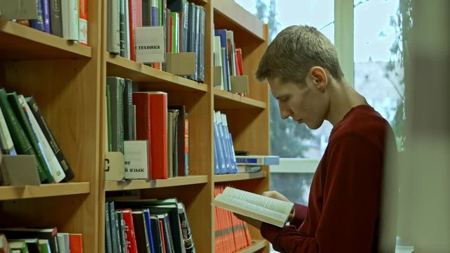 young man in the library searching for a book and listing and reading it