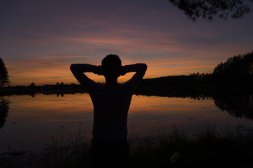 Man looking at sunset  at  the lake holding hands behind his head
