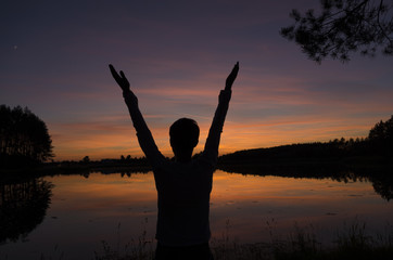 Man greeting sunset standing near the lake and