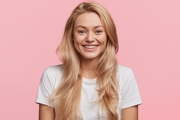 Positive female with appealing appearance has cheerful expression, wears white t shirt, rejoices...
