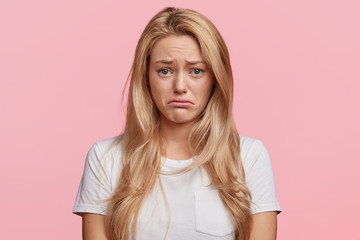 Portrait of displeased upset female frowns face as going to cry, being discontent and unhappy as can`t achieve goals, isolated over pink studio background. Dissapointed young woman has troubles - obrazy, fototapety, plakaty