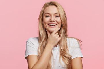Horizontal shot of attractive blonde young female has broad positive smile, demonstrates white...