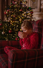 Girl drinking cocoa from a mug by a christmas tree