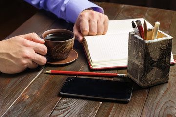 Fototapeta na wymiar Home office workplace, male hand hold a cup of black coffee, smartphone, notepad on dark wood working table, a coffee break time