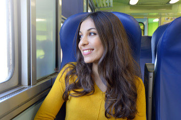 Happy young woman traveling looking out of window while sitting in the train.