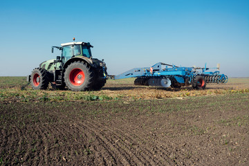 Fototapeta premium Modern tractor in a field on a sunny day. Tractor preparing land for sowing