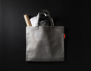 Blank gray fabric shopping bag on black paper background. Flat lay.