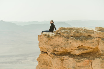 Alone man sitting at the edge of cliff in the desert