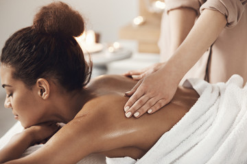 Attractive african girl having massage relaxing in spa salon. Closed eyes.