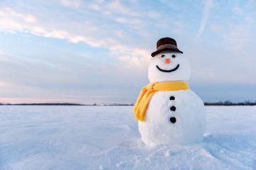 Funny snowman in stylish hat and yellow scalf on snowy field. Merry Christmass and happy New Year!