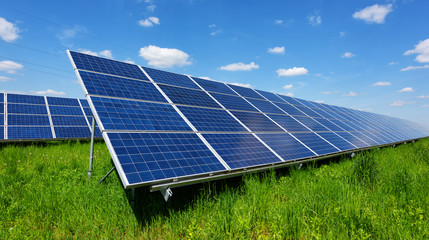 Solar panel on blue sky background. Green grass and cloudy sky. Alternative energy concept