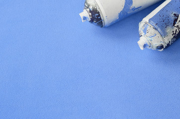 Some used blue aerosol spray cans with paint drips lies on a blanket of soft and furry light blue...