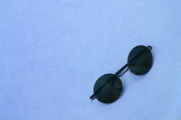 Stylish black sunglasses with round glasses lies on a blanket made of soft and fluffy light blue...