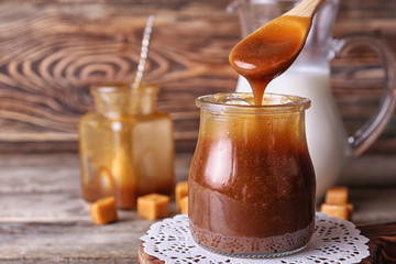 Spoon with tasty caramel sauce over jar on table