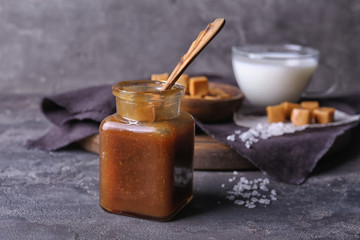 Jar and spoon with tasty caramel sauce on table