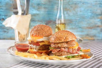 Plate with tasty double burgers on table against wall background