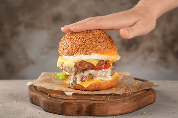 Woman touching tasty double burger on wooden board