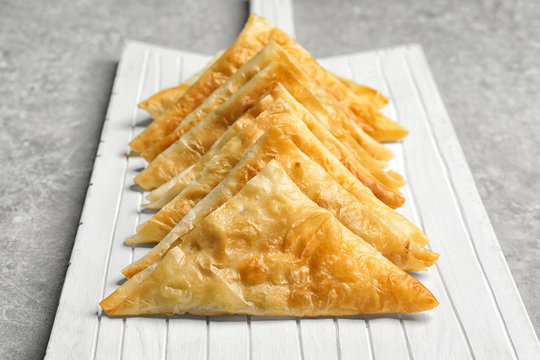 White wooden board with delicious samosas on light background