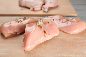 Wooden board with raw chicken fillet on table, closeup