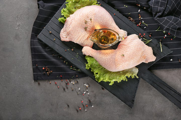 Wooden board with raw chicken legs, oil and lettuce on table
